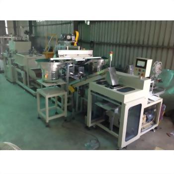 An extensive industrial automation machine, featuring multiple interconnected modules, conveyors, and hoppers, operates within a factory environment.
