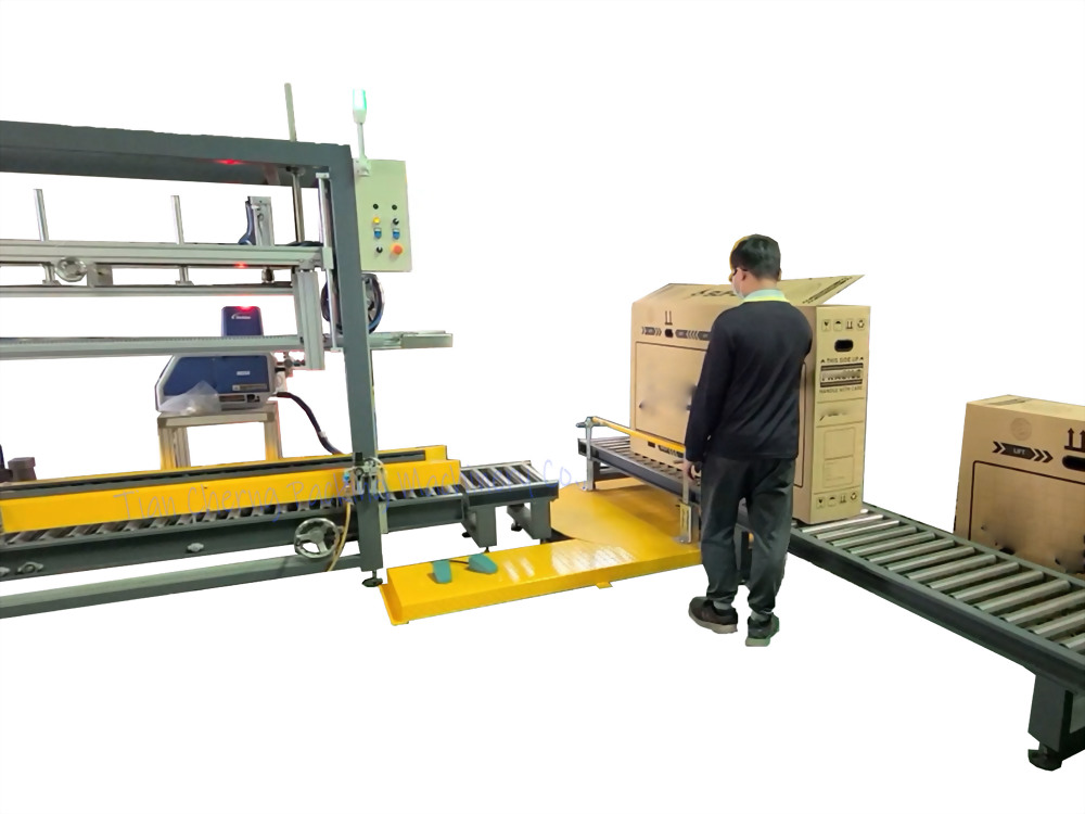 A man places a large cardboard box onto a roller conveyor system next to an industrial packaging machine with a control panel.