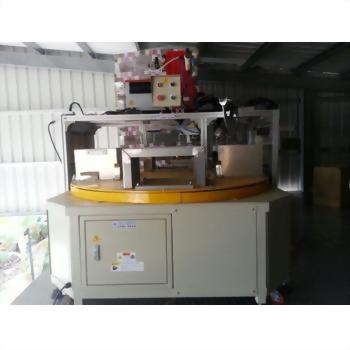 一台米白色工業用自動化機器，配有黃色圓形旋轉平台與上方紅色控制組件，置於室內工作空間。