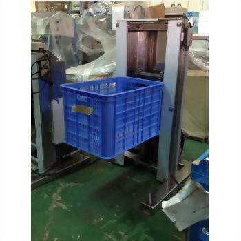 一個藍色塑膠網格籃被銀灰色工業升降機具穩固抬起，背景為工廠內部綠色地板與其他機械設備。