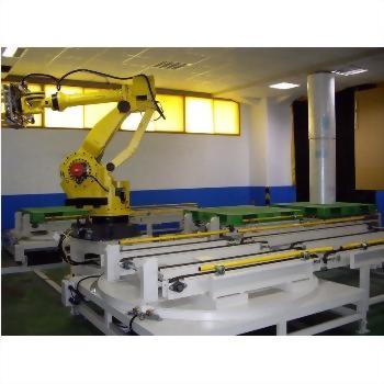 A large yellow industrial robotic arm is positioned next to white conveyor systems with green pallets in a brightly lit factory.